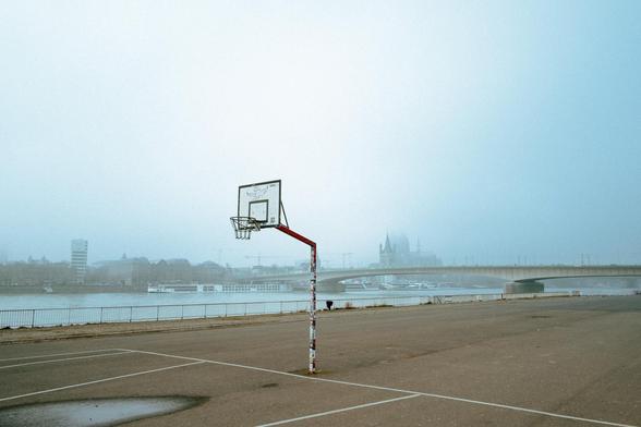 Deutzer Werft im Nebel: Basketballkorb ohne einem einzigen Menschen. Im Hintergrund sieht man den Rhein und den Kölner Dom im Nebel verschwinden.