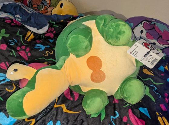 The plush is laying on its side, showing off it's short legs and apple seed like marking on its belly.