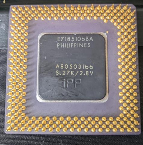 The underside of a 166MHz intel pentium CPU. There are several gold plated pins and a black panel containing product information.