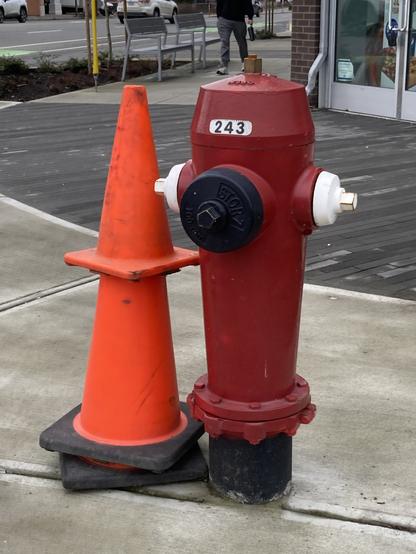 Red hydrant with stacked traffic cones beside it. They are the same height.
