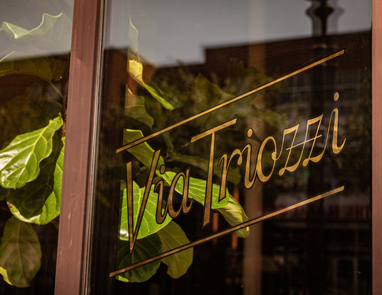 Photo of a restaurant window with “Via Triozzi” in gold gilding.