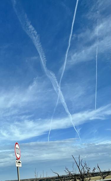 A clear blue sky featuring white contrails from airplanes, with scattered clouds.
