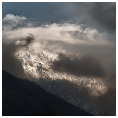 A snow-covered mountain peak visited from swirling clouds, creating a dramatic and majestic scene.