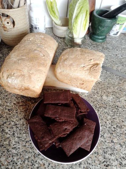 Bourbon biscuits and two loaves of bread on a kitchen bench.