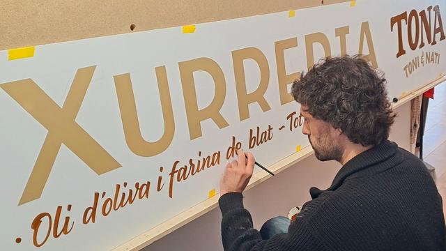 Man painting lettering onto a wide format sign for Xurreria Tona