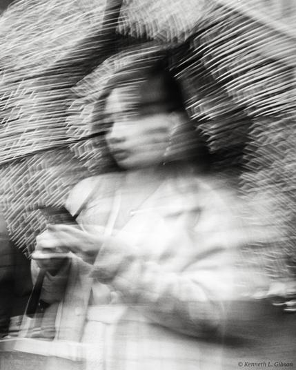 Monochrome intentional camera movement image of a woman with an umbrella and holding a phone.