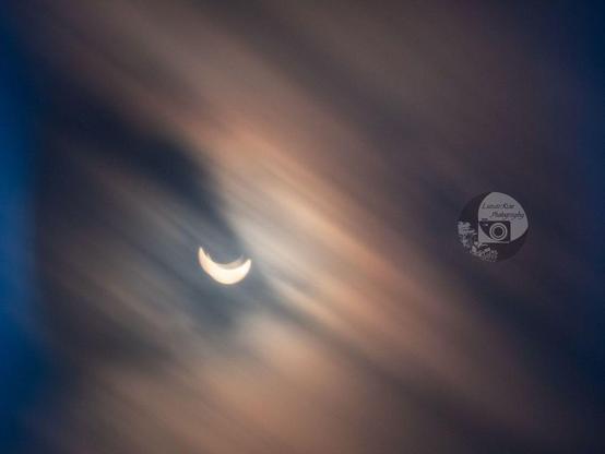 a photo of a partial solar eclipse with motion streaking from the cloud cover. the clouds are refracting the sunlight