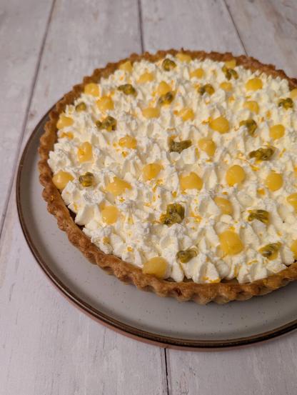 A rectangular photo of the same tart, seen from the side looking downwards. You can see the decoration a bit more - piped stars of whipped cream, with blobs of yellow curd, passion-fruit seeds, and orange zest.