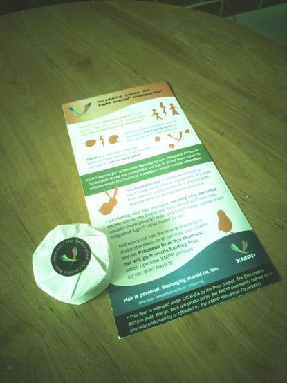 A round shampoo bar wrapped with the XMPP logo, sitting on top of a flyer that will be displayed in detail in the next picture.