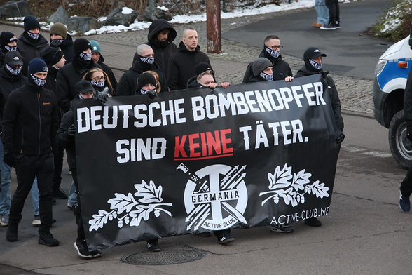 Foto von der Neonazi-Demo am 15.02.25 in Dresden. Vorne ist ein Banner mit der Aufschrift "Deutsche Bombenopfer sind keine Täter - Active Club Germania" zu sehen. Dahinter rechts mittig ohne Vermummung Jann Blumhoff aka. Azatro. Bild von Tim Mönch
