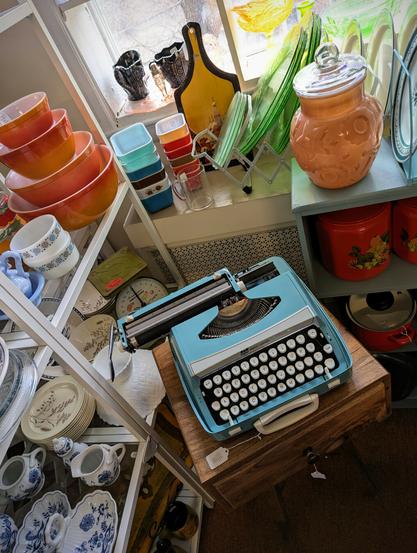 Photo of a variety of mid mod antiques including a light blue manual typewriter, various dishware and Corning ware.