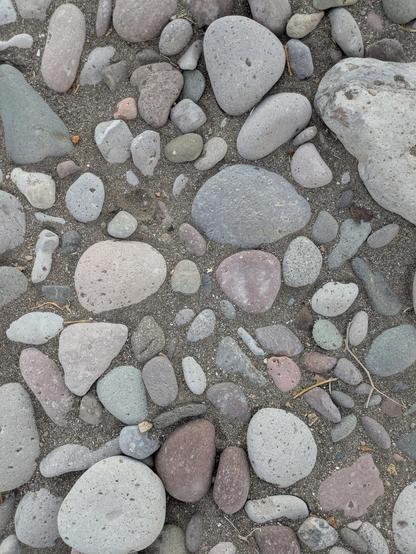 Rocks surrounded by dark sand. The rocks are smooth, ovoid, and with different tones of gray.