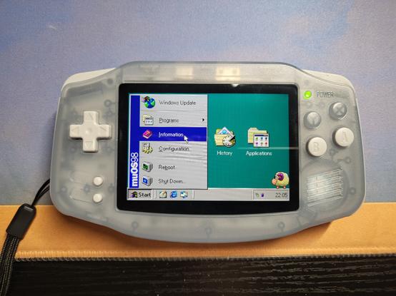 A Retro Handheld shaped like the original Game Boy Advance, displaying a screen that resembles the Windows 98 desktop, and the Start Menu is open. Instead of "Windows 98", the sidebar says "muOS 98", and a menu option called "Information" is highlighted.