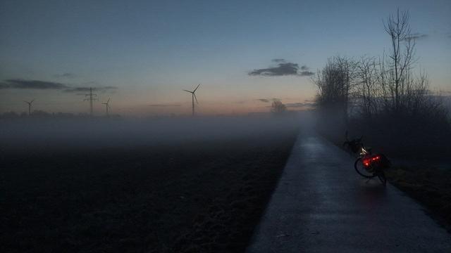 Rad auf Wirtschaftsweg , blauer Himmel bevor die Sonne aufgeht. Nebelschwaden liegen über Feldern und und Weg.