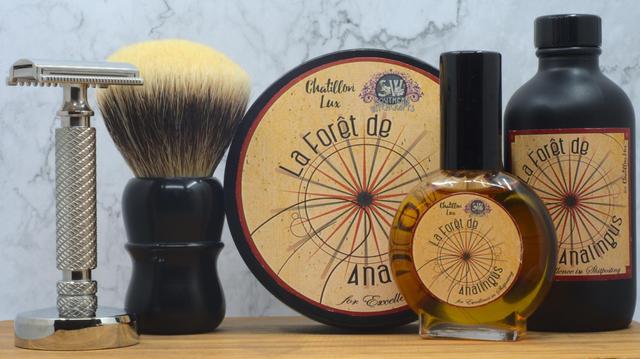 (Le Chat Mistral description)

The image displays a classic shaving set arranged neatly on a wooden surface. It includes a safety razor, a badger hair shaving brush, a round shaving soap container labelled "La Forêt de Analingus" by Chatillon Lux, a matching aftershave bottle, and a smaller bottle of cologne. The items are positioned against a marble-like backdrop, exuding a sense of elegance and tradition in men's grooming. The design of the soap and cologne packaging features a vintage map-like illustration, adding to the set's refined aesthetic.