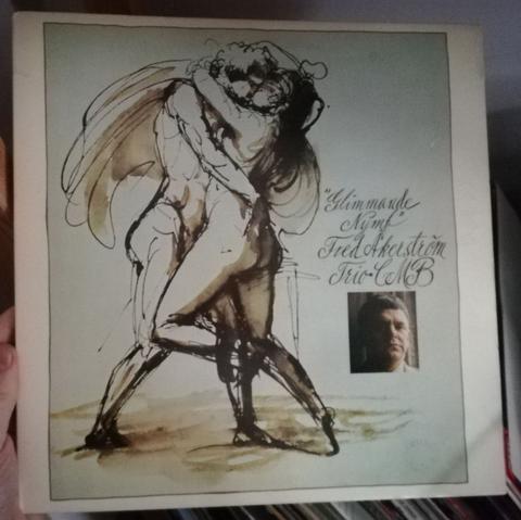 A vinyl cover. An eighteen century drawing of a nude man and a nude woman kissing and embracing. A small picture of a middle aged dark haired man with a winos nose. The handwritten text says: "Glimmande Nymph, Fred Åkerström, Trio CMB"