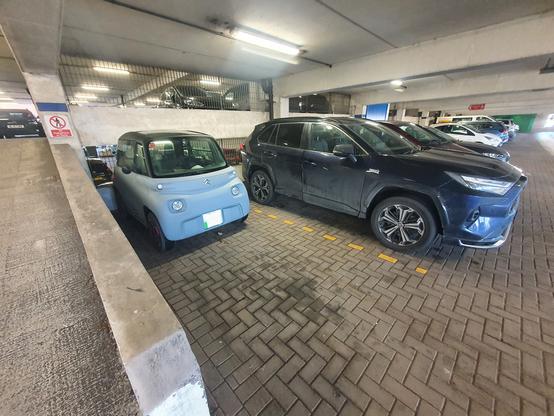 A large car and a small car parked side by side in a multi storey car park.