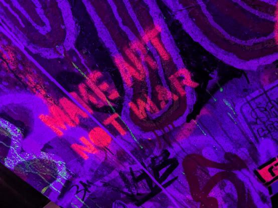 Image: Graffiti-painted wall inside Meow Wolf's Area 15 exhibition facility. Neon stenciled message says "Make Art Not War".