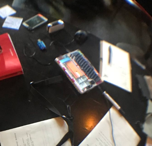 A desk with a clockwork pi devterm computer and papers and a red book, as well as some smaller devices (smartphone, card reader, mouse)