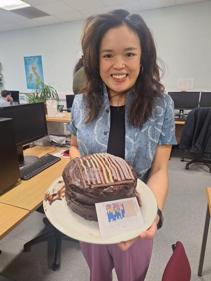 Fiona holding a congratulatory chocolate cake with a mock up of the figure from one of her papers made of sweets