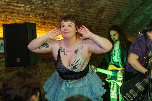 Gen and the Degenerates band on stage. A woman with raised arms, hands turned to her ears, smiling.