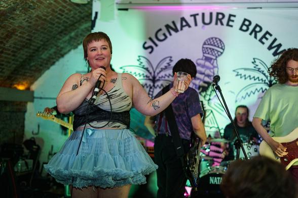 Gen and the Degenerates band on stage. A woman with short hair and in green skirt singing with her band.