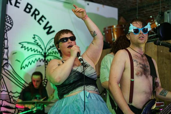 Gen and the Degenerates band on stage. A woman in green skirt and sunglasses raises her arm as she sings into the microphone.