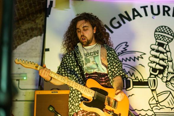 Gen and the Degenerates band on stage. A man with long brown hair playing guitar.
