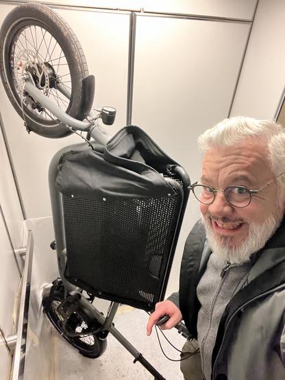 Autoportrait de Tristan et son mini vélo cargo Muli mis à la verticale dans son ascenseur. Tristan fait une drôle de tête : pas facile de tenir le vélo verticalement d'une main tout en faisant un selfie !