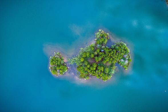 Bild von einer Insel mit grünen Baumen von oben. Um die Insel herum ist türkisblaues Meer.