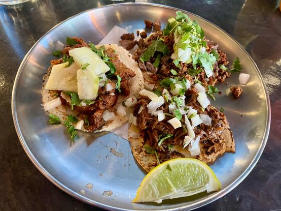 Tacos on a reflective metal platter, fresh cut lime wedge