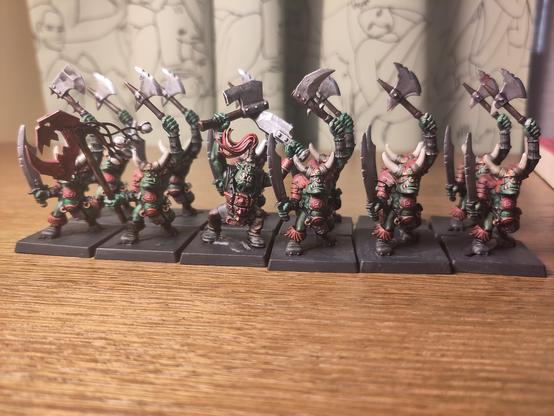 12 turn of the century Games Workshop monopose Orcs wielding swords and axes painted green with red chipped armour. Some conversions to add a banner and repair broken weapons.