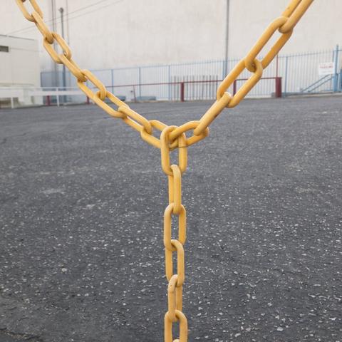 Yellow chain in the shape of a Y in front of a parking lot with red and blue fences in the background