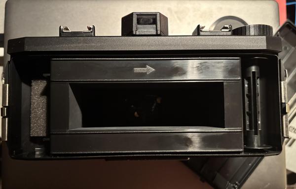 The open back of a panoramic plastic camera, but with the optional 35mm mask in place (to shoot 35mm film with sprockets included). On the left are two nubs which hold the film canister in the center.
