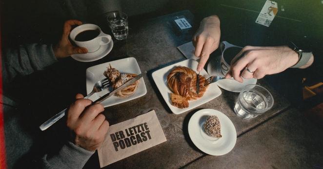 Bild einer schwedischen Fika anlässlich der 500sten Folge von "Der Letzte Podcast". Für eine Fika übliches Gebäck und Kaffee auf einem Tisch. Die Hände von zwei Personen mit Besteck schneiden Zimtschnecken und andere Kuchenteilchen.