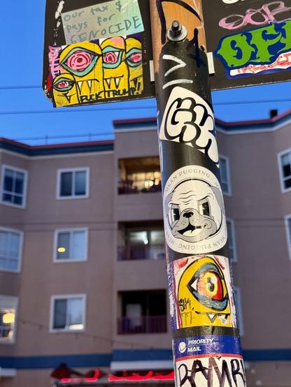 Another photo of the same sign post, but from further away. Here you can see two sticker slaps by Sik. They both feature hand-painted drawings of yellow creatures with sharp teeth.