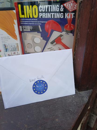 A photograph of a #LINO cutting out and printing set. The envelope is showing a Blue EU flag sticker with peace dove. A note from me "keep faith".