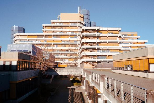 Fachhochschule Deutz: Ein großes verwinkelten Gebäude mit ca 10 Stockwerken die sich treppenförmig nach oben zuspitzen. Viel Beton, gelbe Fläche, geländer und Plateaus. In der Sonne sieht das Gebäude fast ein bisschen Urlaubsmässig aus.