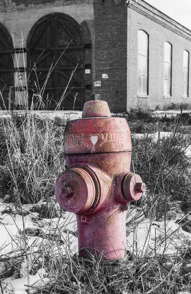 Red fireplug with train yard brick building in background.