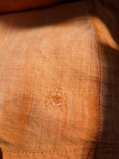 A section of faintly patterned orange garment in sun and shadow, showing a slightly darker orange darn of no artistic merit.
