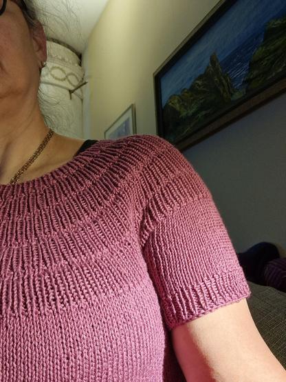 En skymt av en person med en stickad tröja. Av tröjan syns ett ok och en ärm.