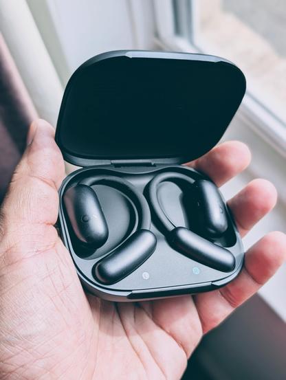 A person holding a pair of black Soundcore Aerofit 2 open earbuds inside a charging case.