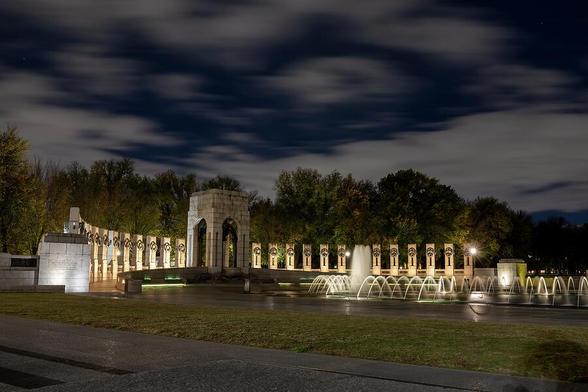 A serene nighttime view of the famous World War II Memorial in Washington, DC, beautifully illuminated with fountains and surrounded by trees, capturing a piece of American history.