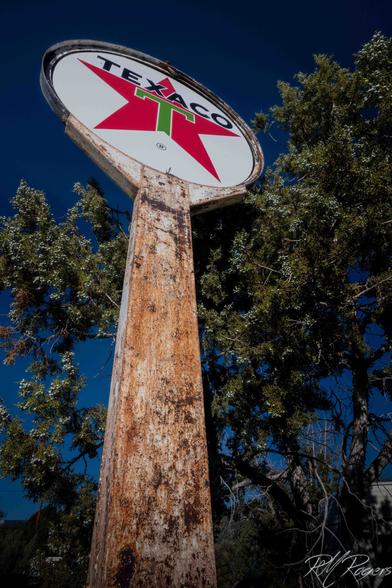 An old rusty Texaco gas station sign towers above Juniper brush in the Utah desert.