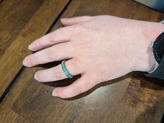 Photo of a woman's hand on a wooden tabletop. She is wearing a tungsten weddingband inlaid with crushed opal.
