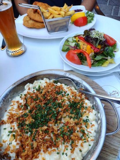 Yummy cheese spaetzle with fried onions and Viennese Schnitzel and a mixed salad along with a glass of wheat beer on a restaurant table.
