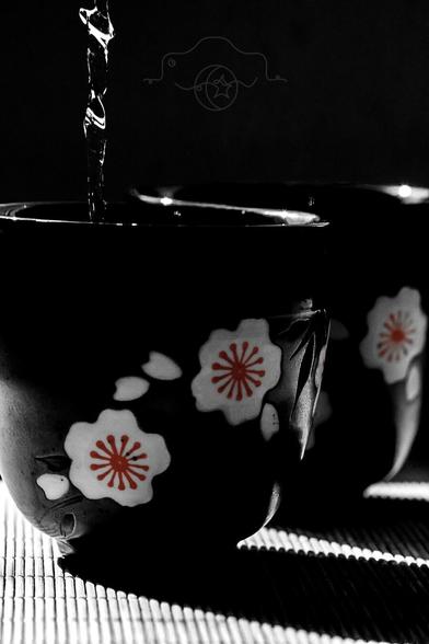 Black & white photo of two tea cups with a pop of red in the painted flowers, with a flow of tea pouring from above.