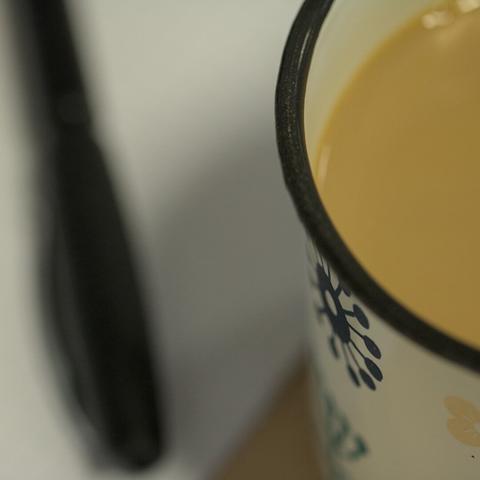 Tasse mit Kaffee. Im Hintergrund ein Stift auf Papier.