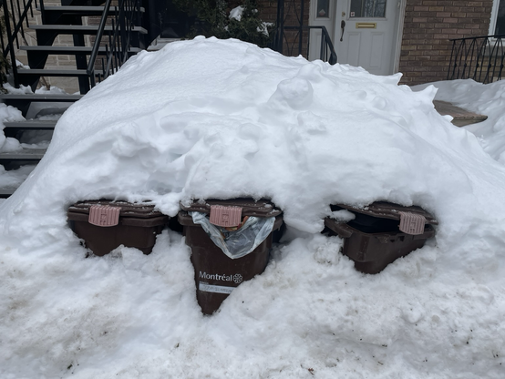 Three compost bins buried under a pile of snow.