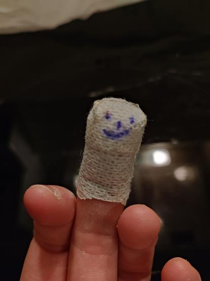 Ein altes Pflaster auf einem Mittelfinger. Auf dem Pflaster ein Smiley.